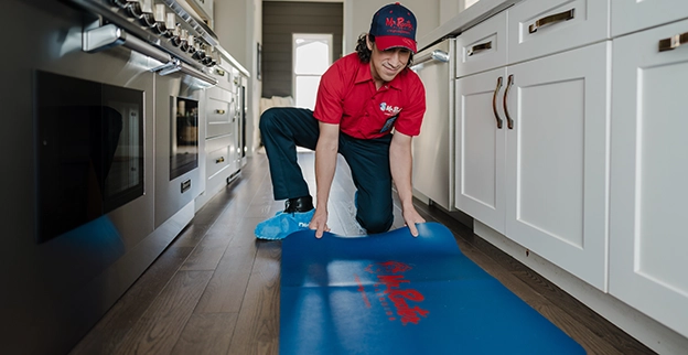 Mr. Rooter professional laying down a mat on a kitchen floor.
