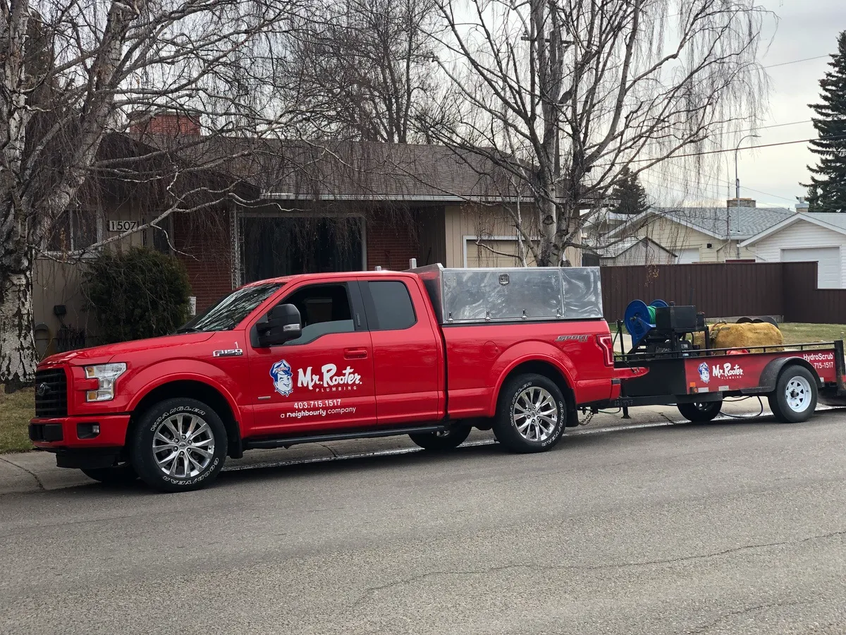 A truck from Mr. Rooter Plumbing with a trailer on the back carrying hydro jetting equipment parked on the street in front of a home receiving plumbing services.