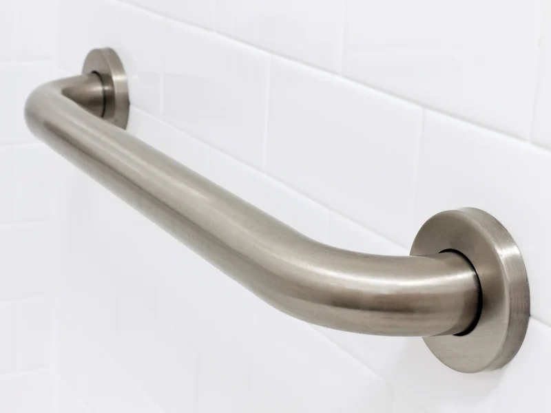 Close-up of a stainless steel grab bar mounted on a white tiled wall, providing support and safety in bathrooms.