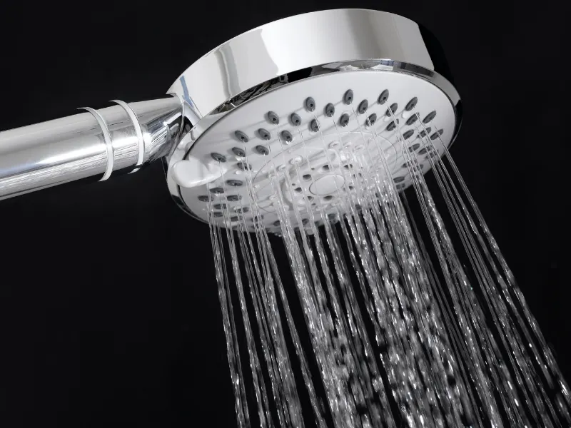 Close-up of a shiny chrome showerhead with water flowing down in multiple streams against a dark background.